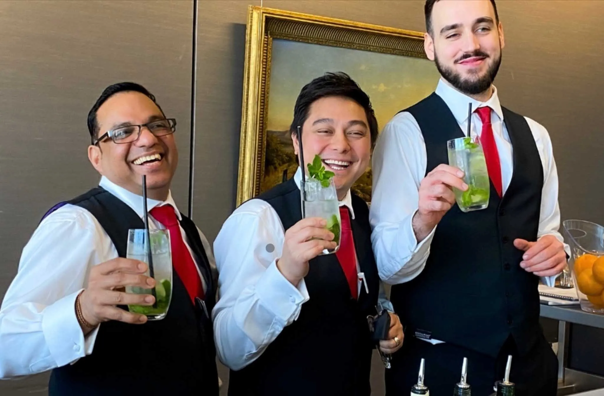 Three men wearing black vests and white shirts are holding drinks.