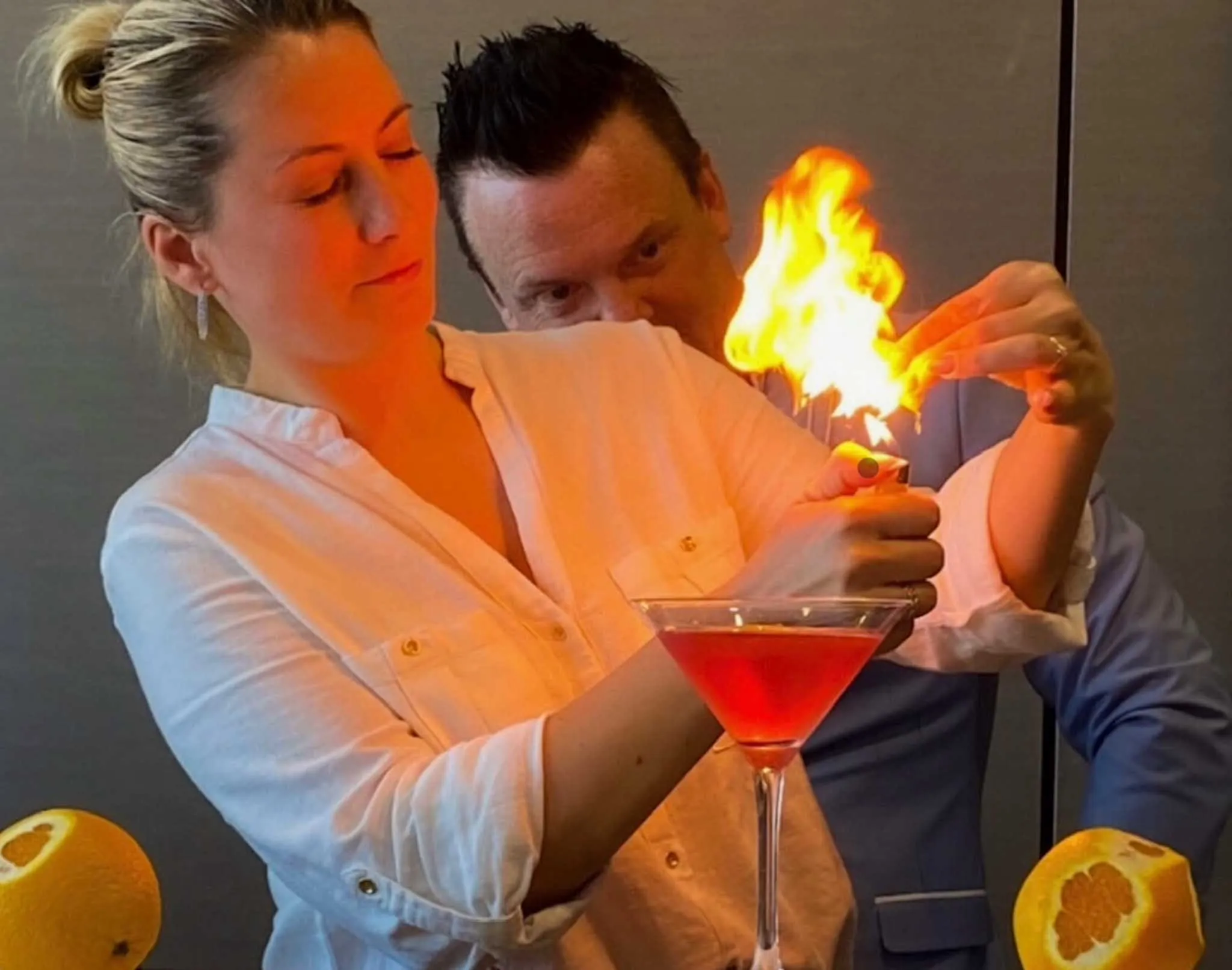 A woman pouring a drink with a flaming orange wedge in it.