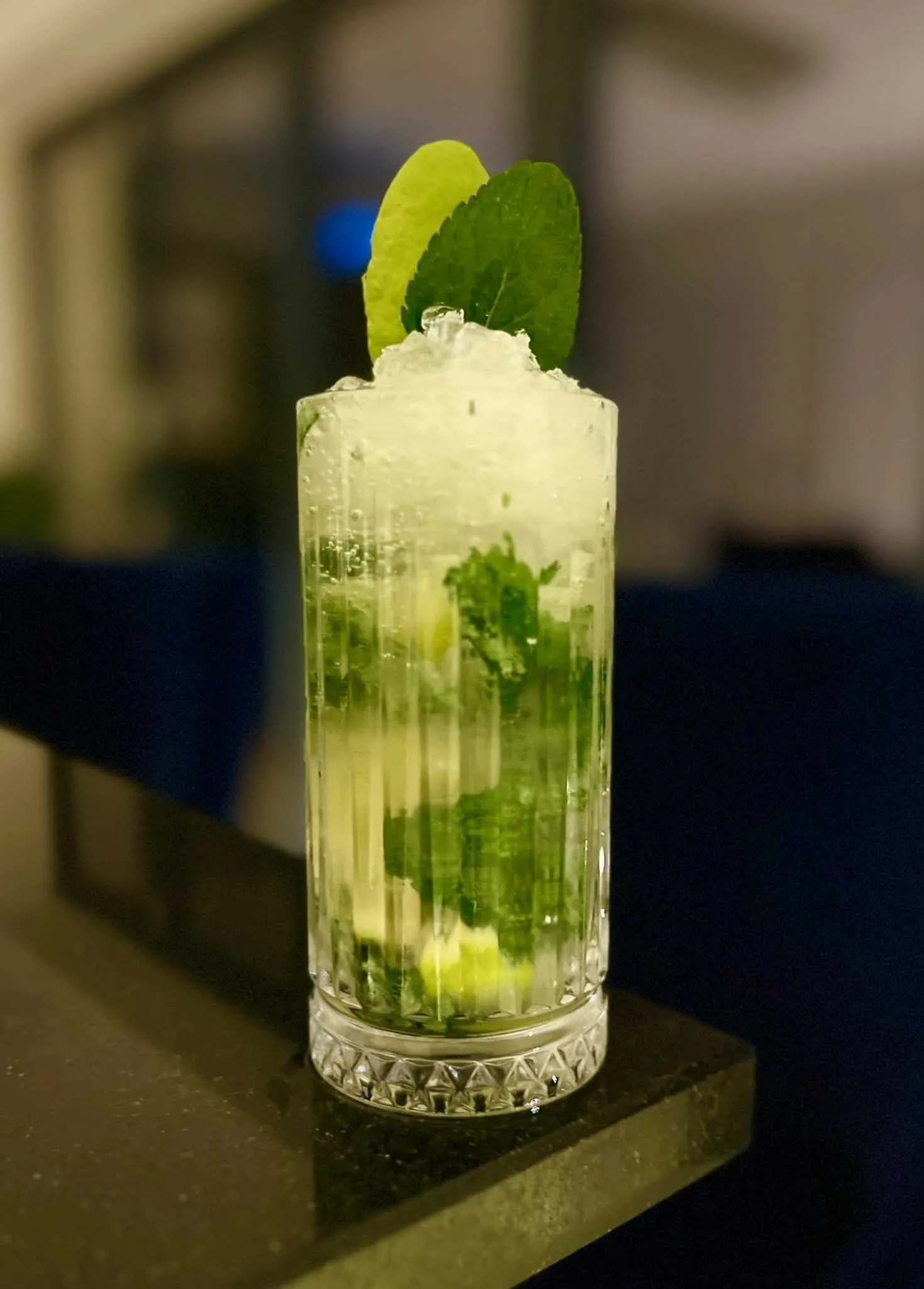 A glass of green drink with a lime wedge on a table.