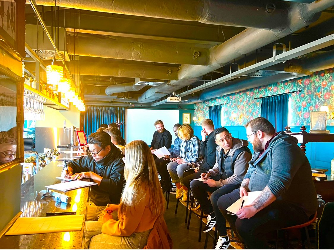 A group of people sitting at a bar with a man in a black shirt writing on a piece of paper.