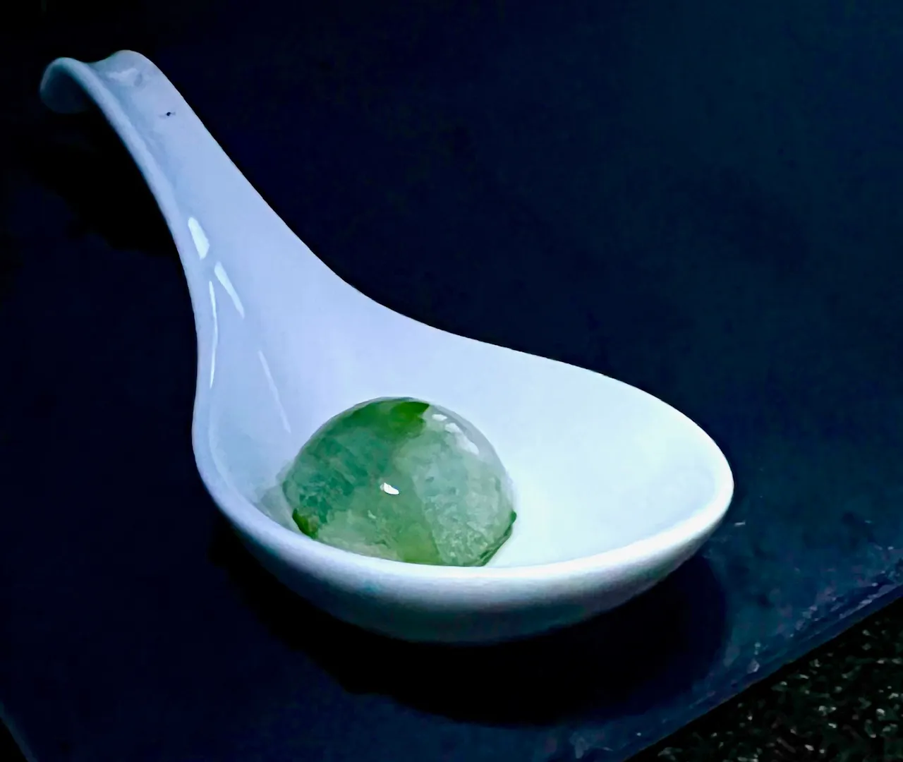 A white spoon with a green stone in it